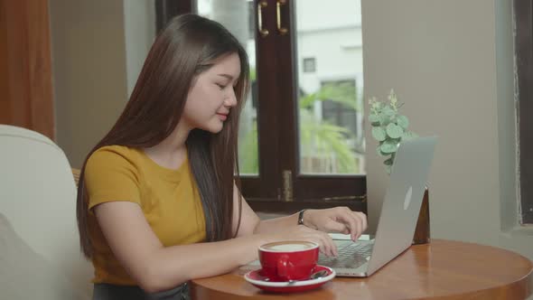 Beautiful Young Asian Girl Working at a Coffee Shop with a Laptop alt