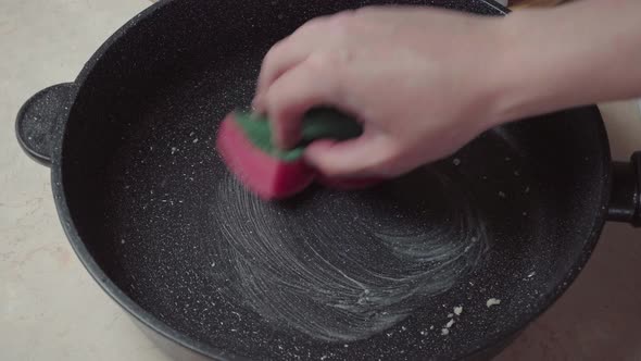 Hand with a foam sponge washes a dirty frying pan. Wash the pan with a sponge alt