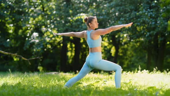 Young woman sportive trainer changes yoga positions stretching on green meadow grass alt
