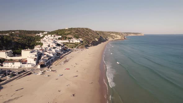Waves washing on sand beach of Salema. White townhouses coastal village in Algarve, Portugal alt