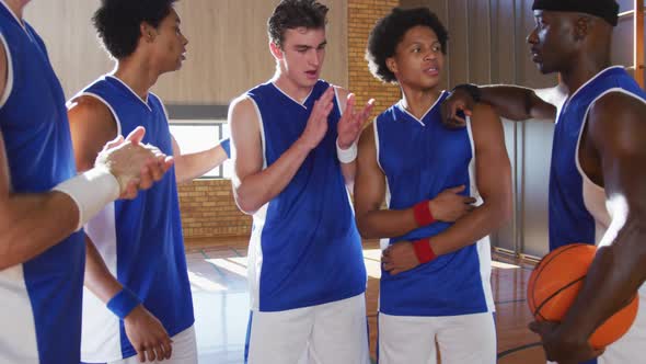 Diverse male basketball team and coach in huddle discussing game tactics alt