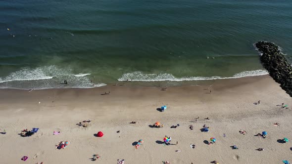 A bird's eye view over people relaxing on the beach on a sunny day. The drone camera truck right & t alt