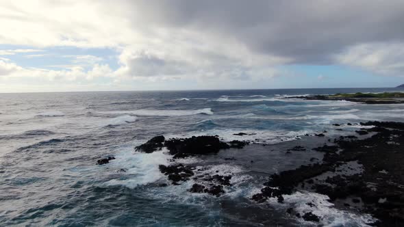 Drone flying above waves crashing on rocky shore in hawaii on a gloomy day alt