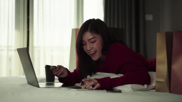 happy woman using tablet for online shopping with credit card on a bed