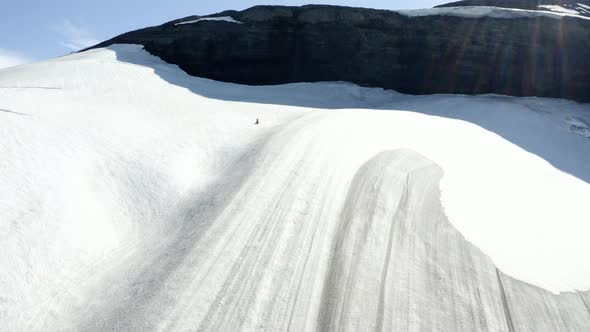 Aerial drone view following a snow mobile on a snowy glacier, in sunny Iceland alt