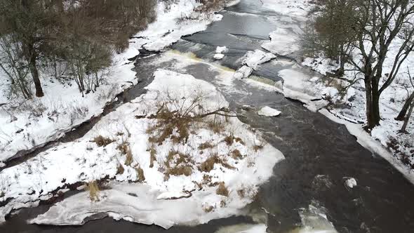 Aerial drone view of a flowing river during winter amongst snowy landscape around. Recorded in Vahik alt