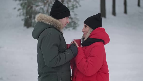 Young Couple in Love Drinking Hot Tea in Winter Forest alt