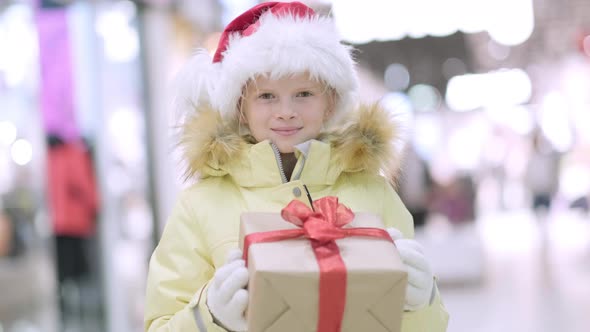 Portrait Winter Little Girl in Santa Hat with Gifts Box in Christmas Shopping Mall Traditional alt