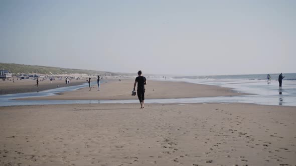 A Man Walks on an Ocean Beach Full of People on a Sunny Day