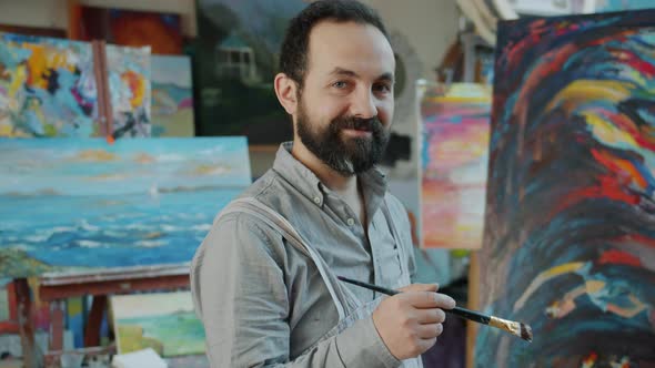Portrait of Handsome Bearded Man Artist Standing in Studio Next To Abstract Picture alt