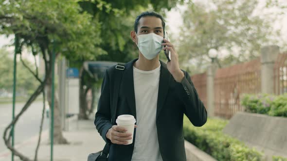 Confident Asian businessman wearing a surgical mask holding coffee cup and talk phone.