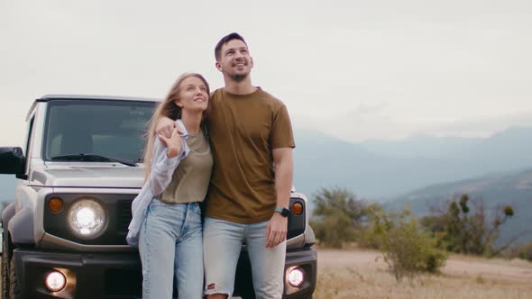 Young Traveler Couple on Road Trip in Mountains Standing Near Car