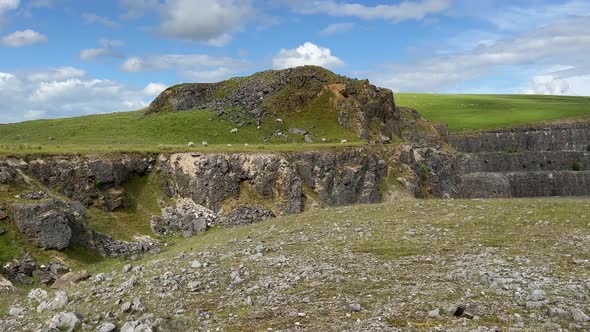 Large hill made from rock with sheep grazing on the grassland and blue sky's alt