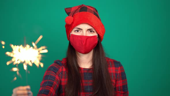 Pretty Woman with Firework Sparkler and Christmas Hat While Wearing Protective Face Mask for alt