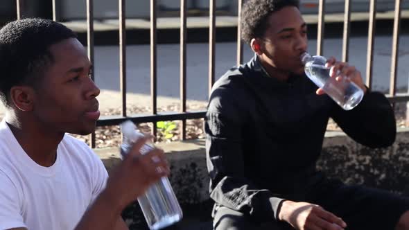 Two young basketball players drinking water while taking a break from playing. alt