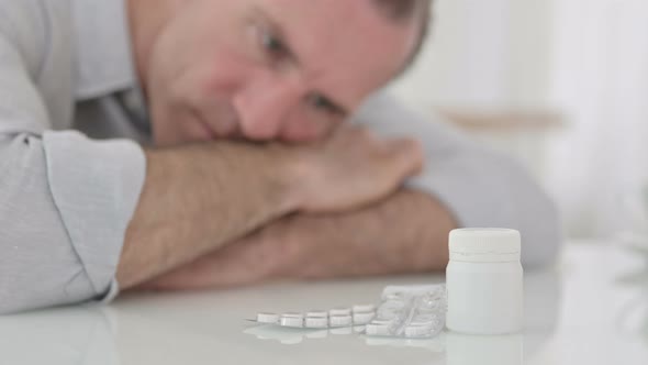 Sick Middle Aged Man Looking at Medicines on a Table  alt
