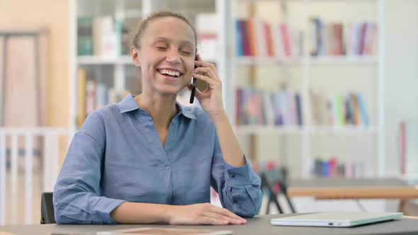 Cheerful African Woman Talking on Smartphone in Library alt