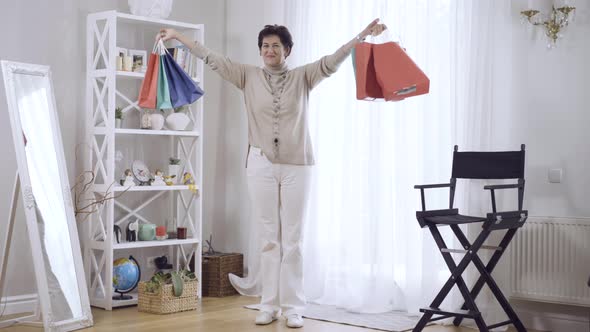 Joyful Middleaged Caucasian Brunette Woman Raising Hands with Shopping Bags and Smiling at Camera alt