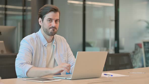 Thumbs Down By Mature Adult Man with Laptop in Office alt