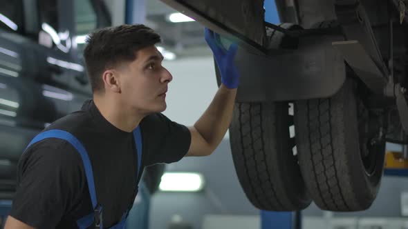 Thoughtful Concentrated Handsome Repairman Checking Auto Parts Under Vehicle alt