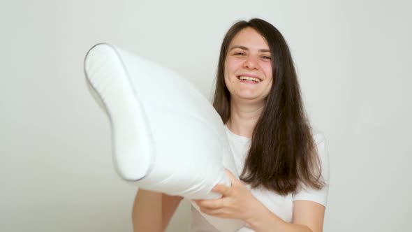 A Happy Woman Throws Up Her Beloved Orthopedic Pillow on a White Background alt