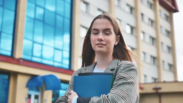 A Young Girl Student Walks Through the City with Folders in Her Hands alt