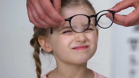 Female Kid Putting on Eyeglasses and Smiling, Optometrist Consultation, Close-Up alt