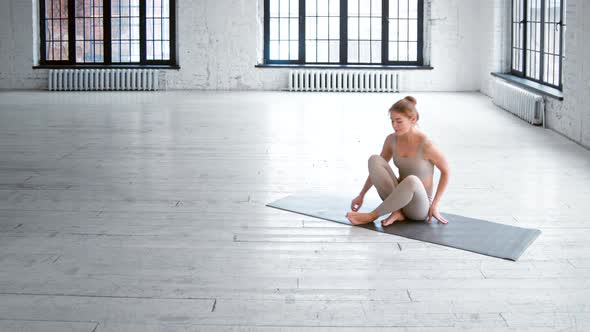 Positive slim young woman in light grey tracksuit comes to mat and sits down in lotus pose alt