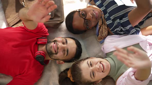 Three Smiling Students Lying on Blanket Waving Looking at Camera alt