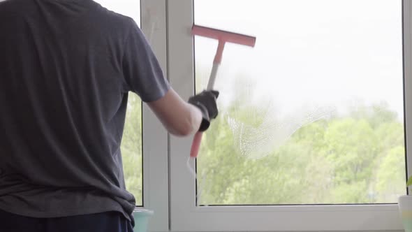 Man washes the windows with special foam and cleans them. Cleaning service. Worker in black gloves alt