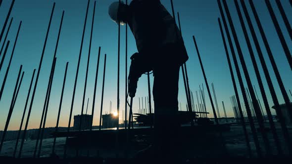Builder Works with a Drill on a Sunset Background. alt