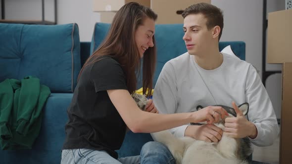 Cheerful Young Couple Playing with Their Dog Indoors alt