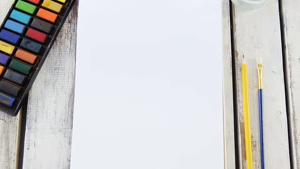 Watercolor paints and paintbrush with blank canvas wooden table alt