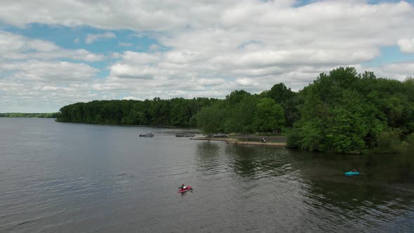 Aerial drone shot of tourists kayaking over a lake beside a park on a cloudy day. alt