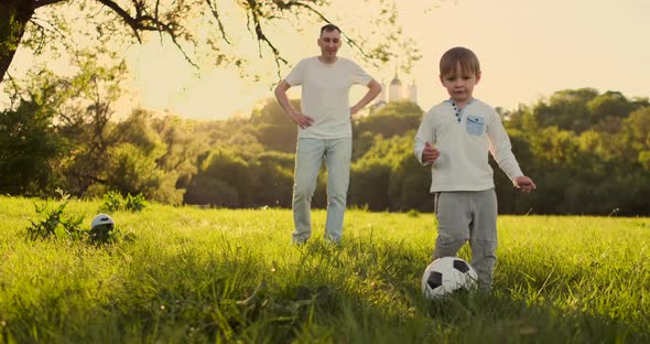Father Standing at the Gate Playing Football with His Son at Sunset alt