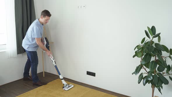 Male Cleaning Floor with Vacuum Cleaner in Modern White Living Room