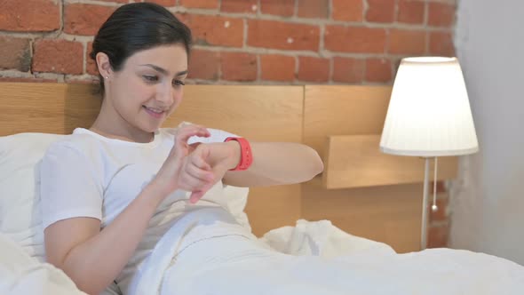Young Indian Woman using Smart Watch in Bed alt
