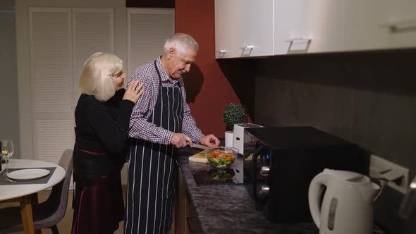 Mature Couple in Love Making Dinner. Elderly Woman Hugging From Back Husband Cooking Meal in Kitchen alt