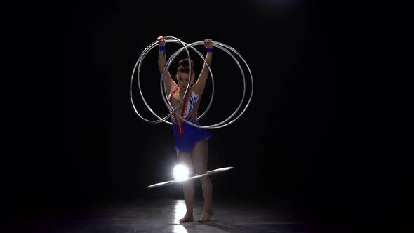 Gymnast in a Bright Outfit Twists a Hoop on Her Arm and Then on Her Leg alt