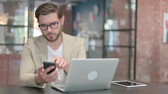 Young Man with Laptop Using Smartphone alt