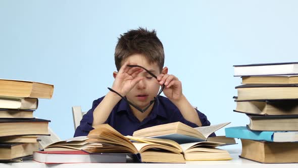 Leepy Little Boy Sitting at a Table and Wearily Leafing Through a Book. Blue Background. alt