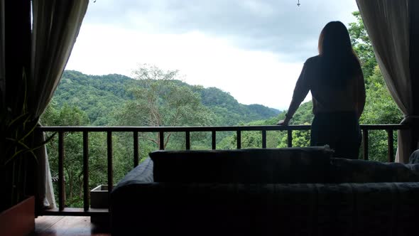 Rear view of a woman standing on balcony and looking at a beautiful mountains and nature view