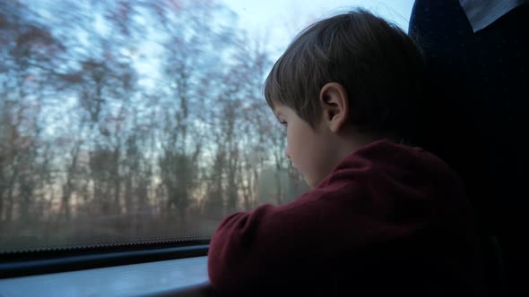 Close-up shot of a little curious boy looking out of the window in train. Its raining outside.