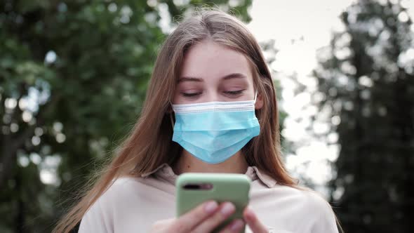 Business woman in medical face mask using smartphone typing message on mobile phone outdoor. alt