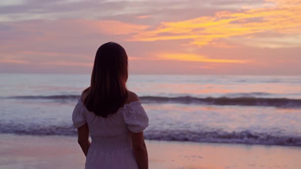 Lonely young Asian woman standing on the beach and looking at the sunset