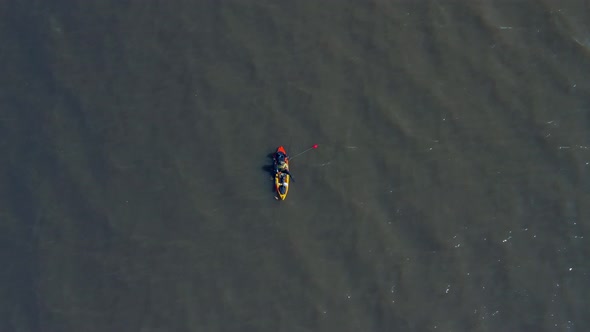 A man in a canoe fishing for food. Calm waters, Aerial, slow movement, top view. River over capital alt