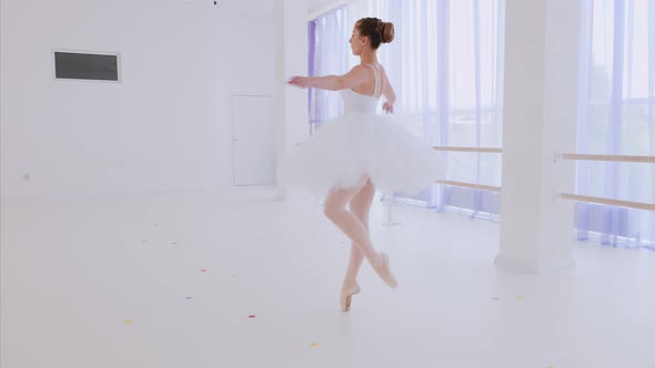 Ballerina in white tutu and pointes is spinning in dance in ballet class.