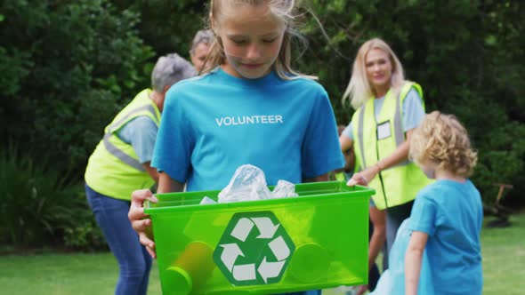 Smiling caucasian girl holding recycling box picking up litter with volunteers in field alt