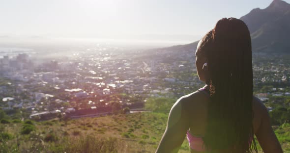 African american woman wearing wireless earphones stretching her arms outdoors alt