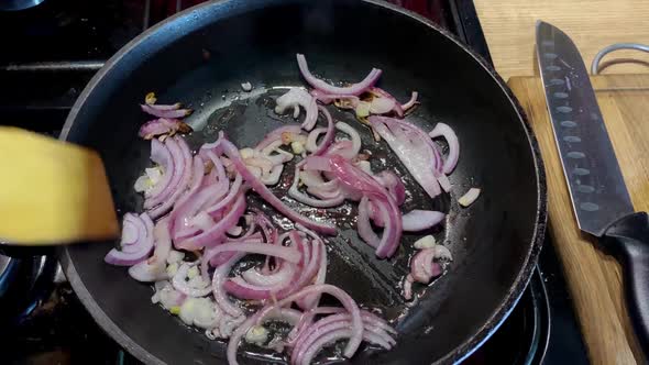 Human Hand Stirring Fried Onion in Frying Pan in Domestic Kitchen for Cooking Food on Kitchen Stove alt